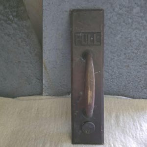 May include: A vintage bronze door handle with the word "PULL" embossed at the top. The handle is a long, oval shape, and a keyhole is visible near the bottom. The handle is mounted on a rectangular plate.
