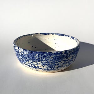 May include: A ceramic bowl with a speckled blue and white design. The bowl has a rounded shape and a smooth, glossy finish. The blue speckles are evenly distributed across the exterior, creating a unique pattern.