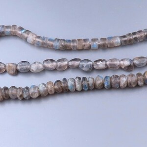 May include: Three strands of labradorite gemstone beads in varying shapes. The beads display a mix of gray, brown, and blue hues. The top strand features small, rectangular beads, while the others have oval and irregular shapes.