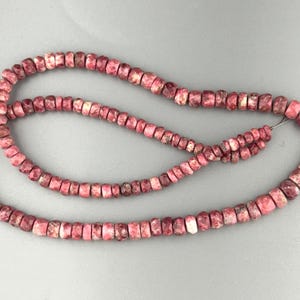 May include: A strand of small, round, faceted beads in shades of mottled pink, magenta, and white. The beads are strung on a thin wire, displaying a natural stone texture with varied color patterns across each individual bead on the strand.