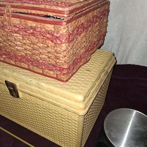 May include: Two vintage woven storage boxes. The top box is reddish-brown with red accents. The bottom box is light yellow with a metal clasp. A digital scale is on the right.
