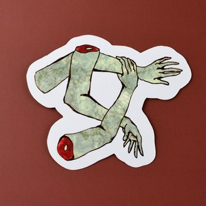 May include: A sticker featuring a pair of green, stylized arms with red accents, intertwined and overlapping. The arms are drawn in a cartoon style and appear to be detached from a body.