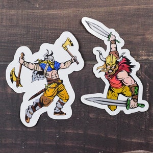 May include: Two colorful cartoon Viking warrior stickers with horned helmets, one holding an axe and the other holding two swords.