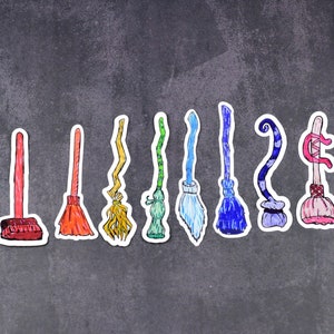May include: A row of nine colourful broomsticks with different styles and designs. The broomsticks are arranged in a line on a grey background.