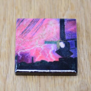 May include: A square ceramic coaster with a pink, purple, and black abstract design. The design features lightning bolts and a cityscape.