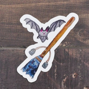May include: A sticker featuring a cartoon bat flying over a blue and brown broom. The bat has pink ears and a gray body. The broom has a brown handle and a blue and white bristle brush.