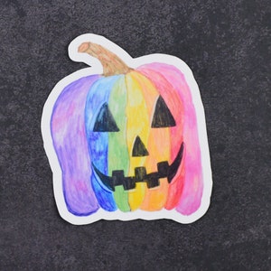 May include: A rainbow-colored pumpkin with a black jack-o'-lantern face. The pumpkin is painted with shades of red, orange, yellow, green, blue, and purple.