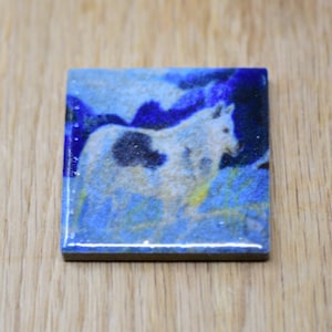 May include: A white and black horse with a blue and yellow background. The horse is in a field of grass and flowers. The image is printed on a ceramic tile.