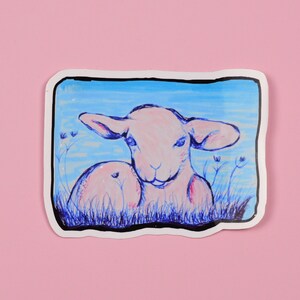 May include: A sticker featuring a hand-drawn illustration of a white lamb with blue eyes, lying in a field of blue flowers. The background is a light blue sky with white clouds.