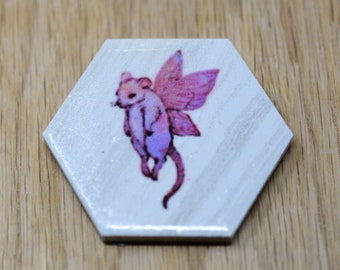 May include: A hexagonal tile with a white background and a pink fairy mouse with wings printed on it.