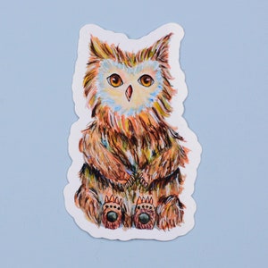 May include: A sticker featuring a cartoon owl with brown, orange, and yellow feathers. The owl has large, round eyes and is sitting with its legs crossed. The owl's feet have brown paw prints.