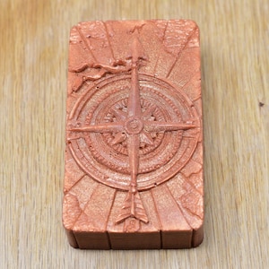 May include: A copper-colored compass with a detailed design, set against a textured background. The compass features a central arrow pointing north and a circular design with radiating lines.