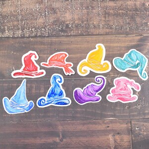 May include: Ten colourful wizard hats with different shapes and designs. The hats are painted in shades of red, orange, yellow, green, blue, purple, and pink.