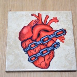 May include: A red anatomical heart with a chain wrapped around it, painted on a beige ceramic tile.
