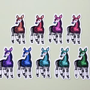 May include: A collection of nine die-cut stickers featuring okapi illustrations in a variety of vibrant colors including red, purple, blue, teal, and green. Each sticker depicts an okapi with its characteristic striped legs and solid body.