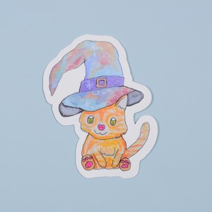 May include: A cute orange cat wearing a purple and blue witch hat with stars and glitter. The cat is sitting with its paws crossed and has a pink nose.