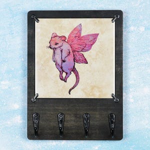 May include: A wooden key holder with four hooks and a framed print of a pink fairy mouse. The frame is black and the hooks are black metal.