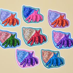 May include: A collection of eight die-cut stickers featuring hermit crabs in various colors including orange, pink, green, purple, and blue. Each crab is depicted emerging from a spiral shell with distinct patterns and textures in a cartoon style.
