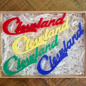May include: Four "Cleveland" signs in a box, each in a different color: red, yellow, green, and blue.