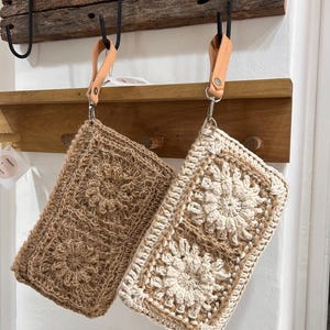 May include: Two crocheted bags hanging on a wooden rack. The bag on the left is brown and the bag on the right is white and brown.