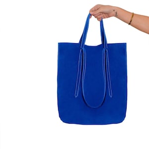 以下が含まれることがあります： 白いステッチが施された明るいブルーのトートバッグ。バッグは柔らかく、質感のある生地で作られています。