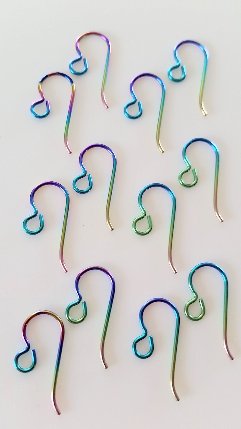 May include: Ten rainbow-colored earring hooks, made of metal, are arranged on a white surface. The hooks are all the same size and shape, and they have a slight curve at the top.