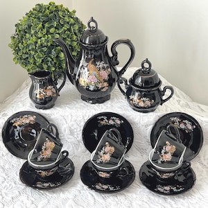 May include: A black and gold tea set with a teapot, creamer, sugar bowl, and four cups and saucers. The set features a floral and bird design.