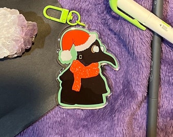 Può includere: Un portachiavi a tema natalizio verde e rosso con un dottore della peste dei cartoni animati che indossa un cappello di Babbo Natale e una sciarpa rossa.
