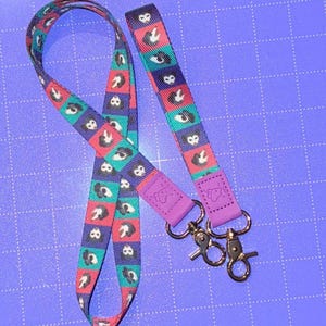 May include: A patterned lanyard with a repeating design of black and white animal print shapes on a teal, red, and purple background. The lanyard has a purple strap with a silver clasp.