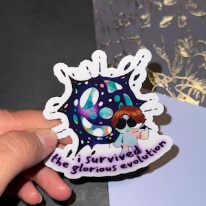 May include: A white sticker with a colorful galaxy design and a cartoon character. The text on the sticker reads "I survived the glorious evolution."