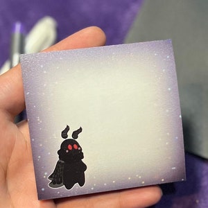 May include: A purple sticky note with a black and red cartoon moth with three eyes. The background of the note has a subtle sparkle effect.