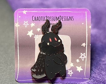 May include: Black enamel pin featuring a cartoon moth with pink accents and a starry background. The pin is on a card with the text "CHAOTICROSSUMDESIGNS".