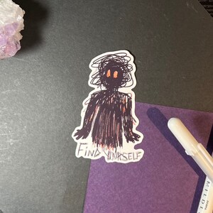 Op de afbeelding: Een zwart-witte sticker met een eenvoudige lijntekening van een persoon met oranje ogen. De tekst "Find Yourself" staat onder de tekening.