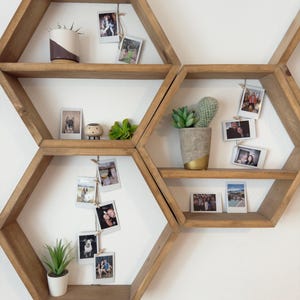 May include: A set of six hexagonal wooden shelves with a natural wood finish. The shelves are arranged in a honeycomb pattern and are decorated with potted plants, small figurines, and framed photos.