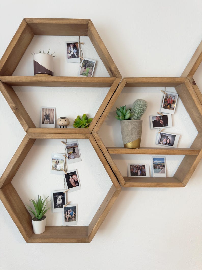 May include: A set of six hexagonal wooden shelves with a natural wood finish. The shelves are arranged in a honeycomb pattern and are decorated with potted plants, small figurines, and framed photos.