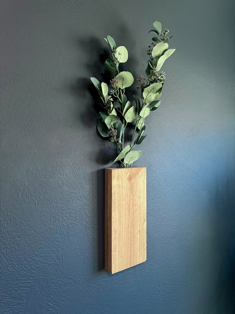 Op de afbeelding: Een houten wandvaas met een natuurlijke houten afwerking bevat een tak met groene eucalyptusbladeren.