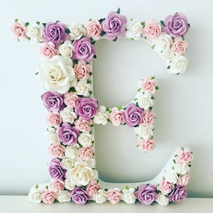 K&ouml;nnte beinhalten: Ein wei&szlig;er Buchstabe E, der mit rosa, wei&szlig;en und lila Blumen verziert ist. Der Buchstabe besteht aus Schaumstoff oder Pappe und ist mit k&uuml;nstlichen Blumen bedeckt.