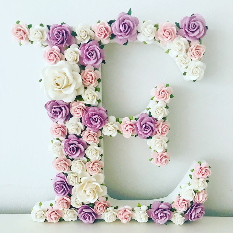 K&ouml;nnte beinhalten: Ein wei&szlig;er Buchstabe E, der mit rosa, wei&szlig;en und lila Blumen verziert ist. Der Buchstabe besteht aus Schaumstoff oder Pappe und ist mit k&uuml;nstlichen Blumen bedeckt.