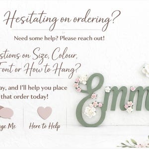 May include: Sage green wooden name sign, "Emmy", decorated with delicate floral accents. The name is styled in a cursive font and decorated with small, light pink and white flowers. The image also contains text.