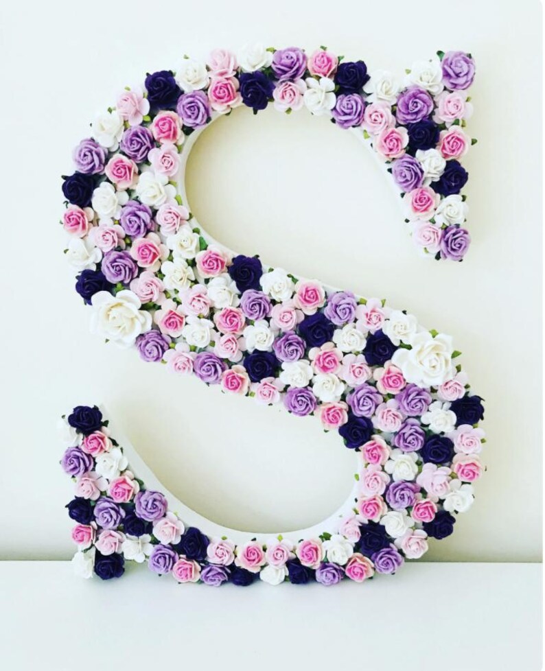 K&ouml;nnte beinhalten: Ein wei&szlig;er Buchstabe S, der mit kleinen k&uuml;nstlichen Blumen in Rosa-, Lila- und Wei&szlig;t&ouml;nen bedeckt ist.