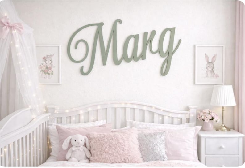 May include: A child's bedroom with a white cot and pink bedding, including cushions and a stuffed bunny. A large, cursive "Marg" sign in green is on the wall, alongside framed bunny and floral artwork.
