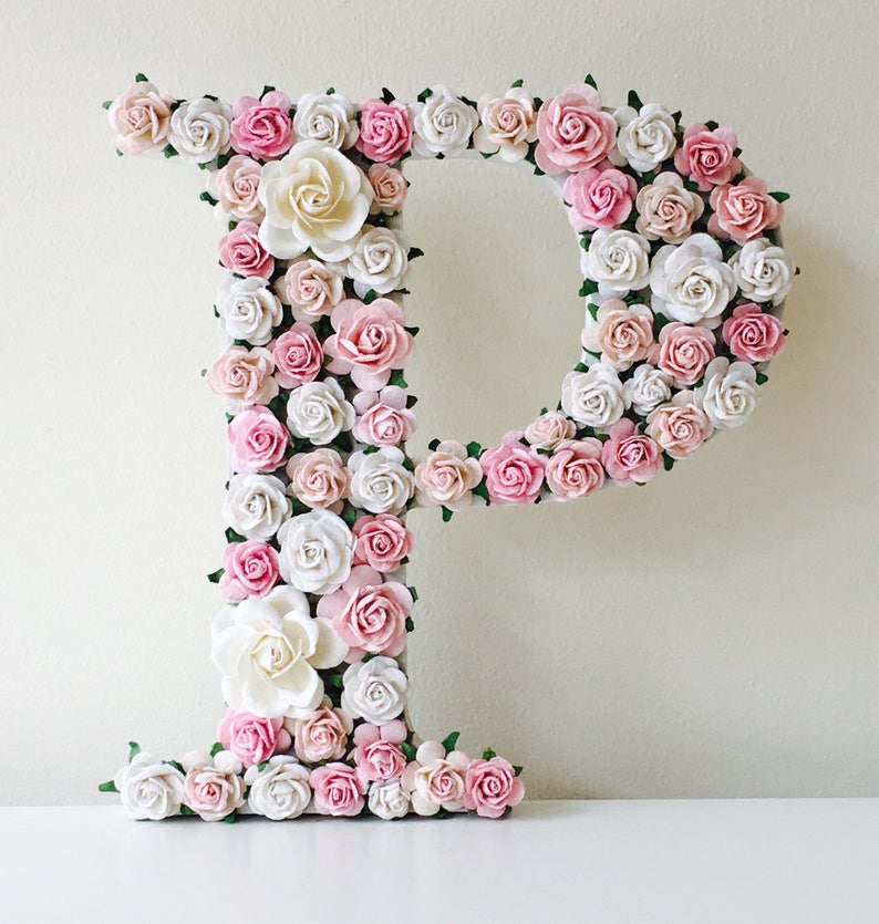 Pode incluir: Uma grande letra P feita de flores de papel rosa e branco. A letra &eacute; decorada com pequenas folhas verdes.