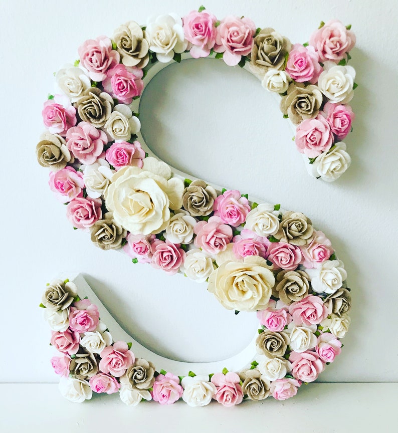 K&ouml;nnte beinhalten: Ein wei&szlig;er Holzbuchstabe S, der mit rosa, wei&szlig;en und braunen Papierblumen verziert ist. Die Blumen sind in einem Kreis um den Buchstaben angeordnet.