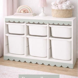 May include: A white storage unit with six compartments, each containing a white bin. The unit features a scalloped trim in a pale green. A pink lamp and a basket of soft toys sit on top. The text "Bramwell green" is at the bottom.