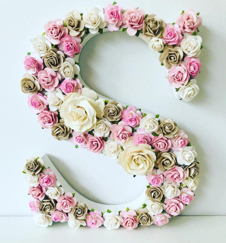 Pode incluir: Uma letra S de madeira branca decorada com flores de papel rosa, creme e marrom. A letra &eacute; um elemento decorativo para um ber&ccedil;&aacute;rio ou decora&ccedil;&atilde;o de casa.