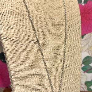 May include: A silver-toned necklace with a square, clear crystal pendant. The pendant is set in a silver metal frame and hangs from a delicate chain. The necklace is displayed on a beige bust form.
