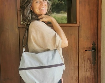 May include: A light gray shoulder bag with a brown zipper and strap. The bag is made of a textured fabric and has a rounded shape. The strap is a dark brown color.