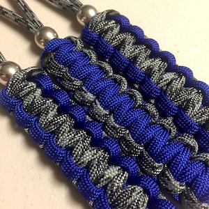 May include: Three blue and grey paracord keychains with silver beads. The keychains are made with a braided paracord pattern.