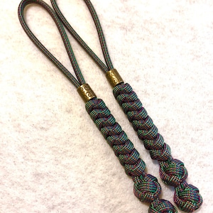 May include: Two green, red, and black braided paracord keychains with a brass bead and a knot at the end.