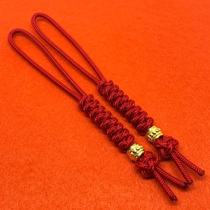 May include: Two red string bracelets with gold beads. The bracelets are tied together with a knot.